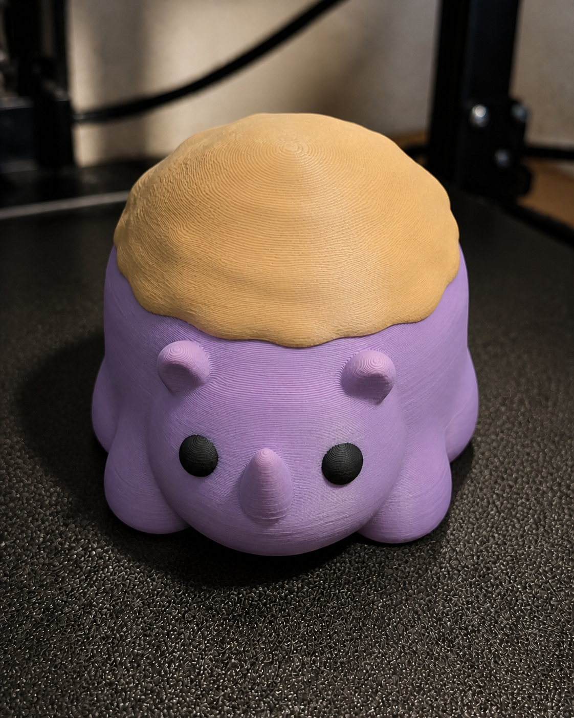 A chunky purple and tan muffin rhinoceros Artwork Figure on a 3D-printer build plate